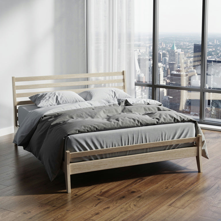Wooden bed with gray bedding in a room with large windows showing a cityscape.