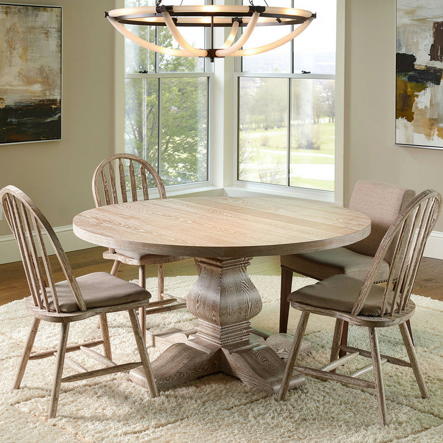 Round dining table with chairs in a well-lit room with large windows.