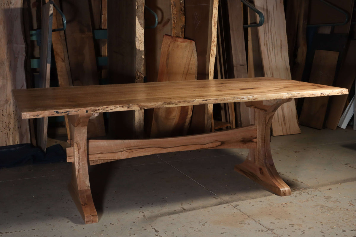 Elegant Finn trestle dining table with solid wood construction, featuring a curved base and natural finish, perfect for any style.