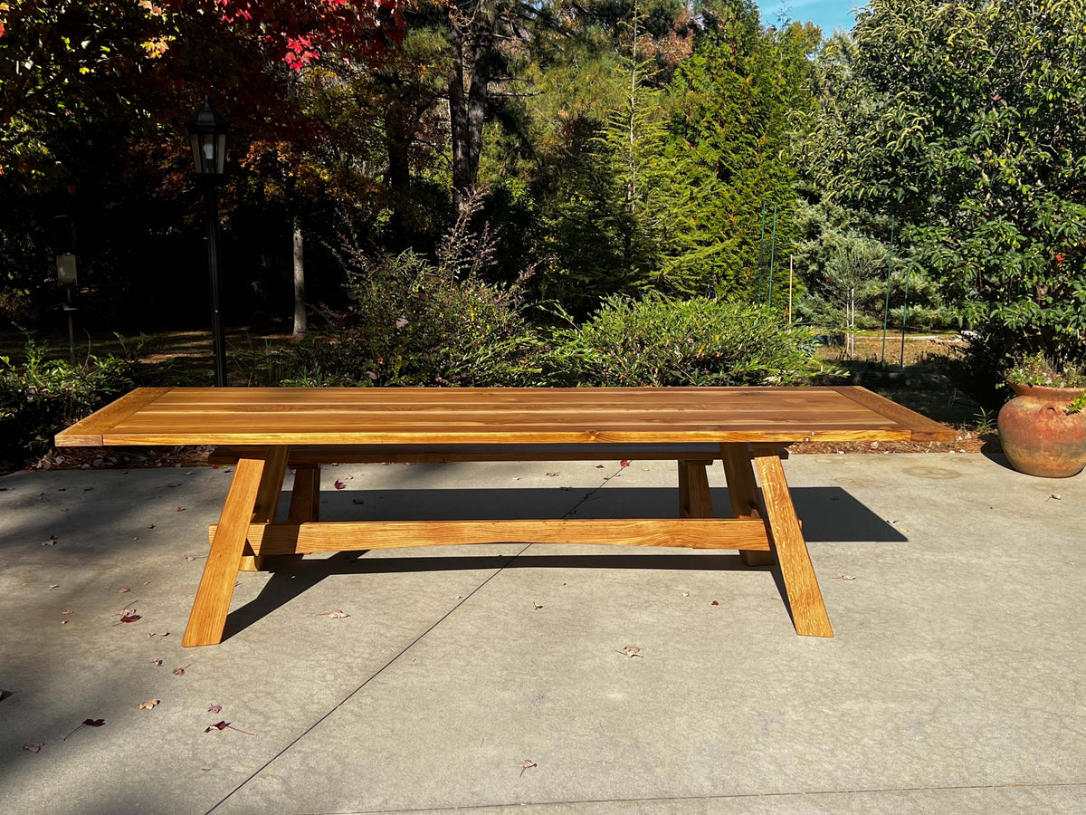 The Nikko Dining Table in sunlight with Japanese-inspired design, reflecting sun rays on a patio with lush greenery in the background.