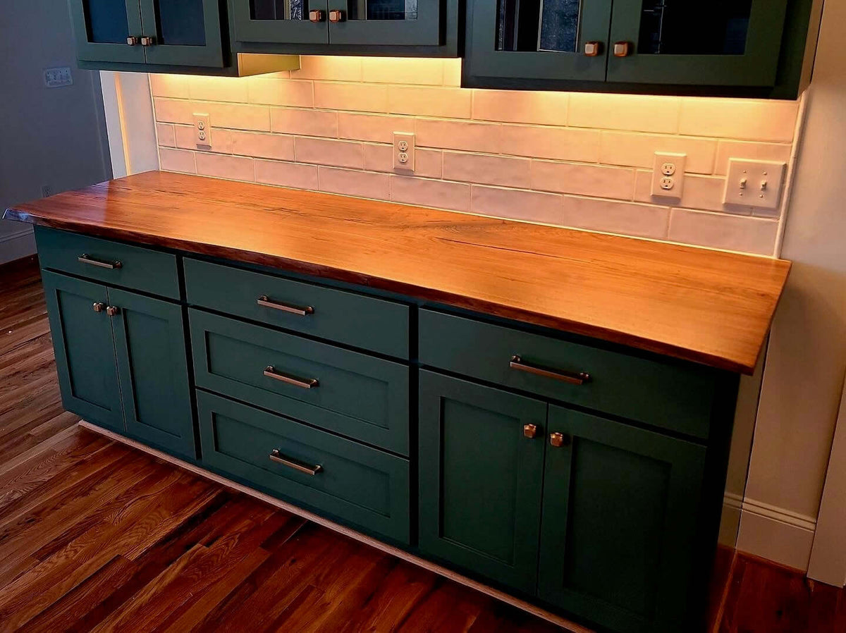 Live edge wood countertop on green cabinets in a modern kitchen setting.