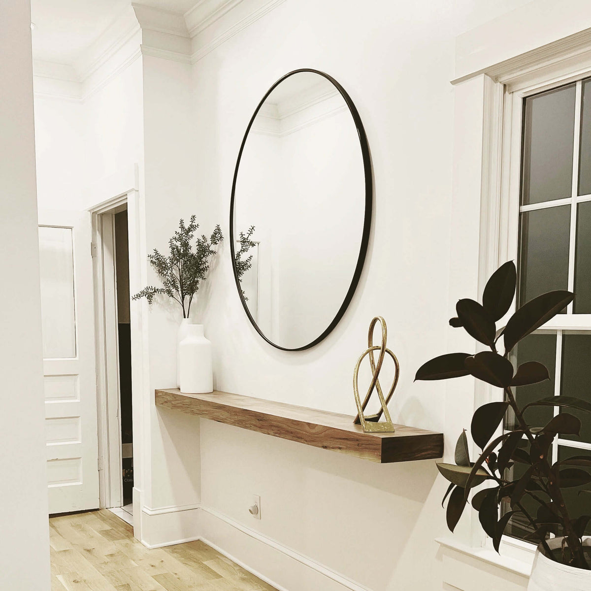 Modern hallway with faux beam mantle, round mirror, and decorative plants.